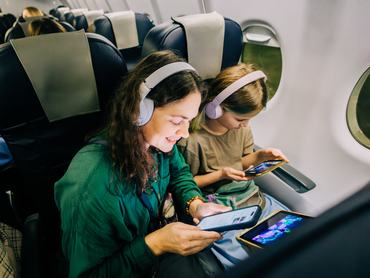 Anya és lánya repülőgépen utazik digitális eszközökkel és fejhallgatóval