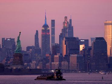 Egy vontatóhajó uszályt tol a Szabadság-szobor és az Empire State Building előtt naplementekor New Yorkban 2026. május 25-én, a New Jersey állambeli Bayonne-ból nézve.