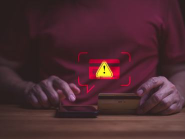 Egy férfi okostelefonnal akar online fizetni. A kép fizetési csalásra figyelmeztet.