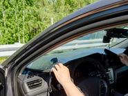 egy nő éppen hővédő fóliát tesz fel a kocsi szélvédőjére, az ajtó már nyitva van, hamarosan kiszáll