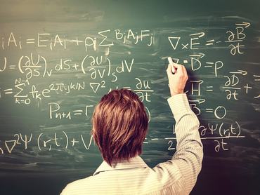 Newton's Equations. Rear view, close-up on young man standing back against green chalkboard. He explains, solves physics tasks, retro style. Processing for retro bleached look, slight vignette added.