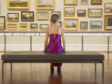 Egy nő a múzeumban ülve nézi a festményeket