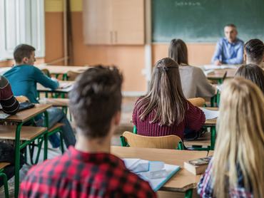 tanulók ülnek a teremben a padokban, előttük, szembe velük a tanár