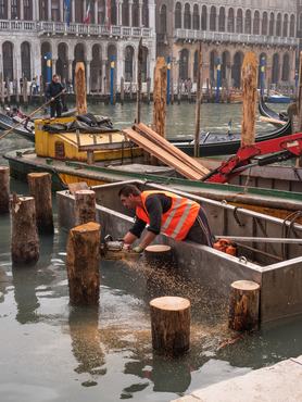 Venice, Italy - October 13, 2017: A new berth for gondolas and boats is under construction. The worker saws the hammered piles to the same height. After that, the flooring is done.