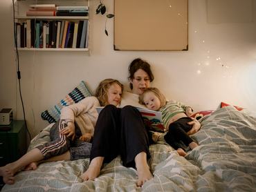 Egy anya az ágyon ülve mesét olvas két gyerekének