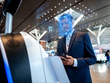 Üzletember áll egy repülőtéri utasfelvételi terminálnál, miközben az arcfelismerő technológia digitálisan beolvassa az arcát