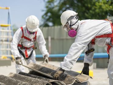 Az azbeszttető eltávolítása során védőruházatot viselő munkások. A veszélyes hulladékok kezelésére és a munkavédelemre vonatkozó koncepció. Szakszerű hulladékártalmatlanítás.