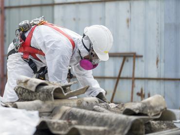 Az azbeszttető eltávolítása során védőruházatot viselő munkások. A veszélyes hulladékok kezelésére és a munkavédelemre vonatkozó koncepció. Szakszerű hulladékártalmatlanítás.
