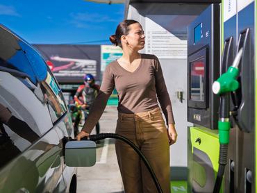 Egy nő megtankolja az autóját a benzinkúton és az üzemanyag árát nézi a kijelzőn