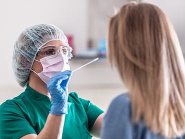 Egy védőruhát és maszkot viselő egészségügyi dolgozó mintát vesz egy fiatal szőke nőtől, hogy megállapítsa a Covid-19-fertőzést