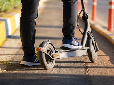 Egy elektromos robogón ülő férfi lábainak hátsó nézete a kerékpársávon, a szabadban.