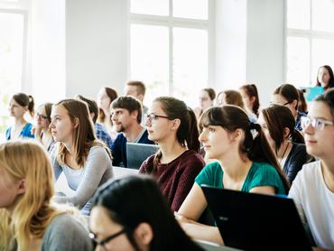 Egy csoport hallgató figyelmesen hallgatja az oktatót egy egyetemi előadáson.
