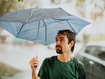 Egy férfi esernyőt tart a feje fölé az esőben