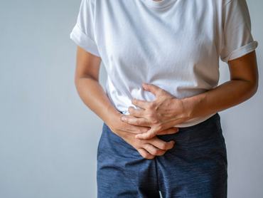 Egy fiatal nő, aki az alhasát fogja, görcsök vagy hasfájás miatt szenved.