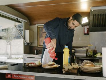 Egy szakács, aki a food truckjában főzés közben ketchupot tesz egy vendég hamburgerére.