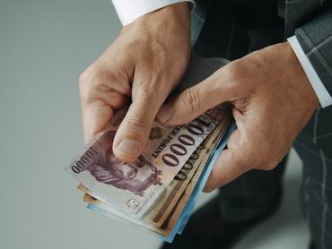 Közelkép egy elegáns szürke öltönyös üzletemberről, aki néhány magyar forintos bankjeggyel a kezében áll egy beltéri helyiségben
