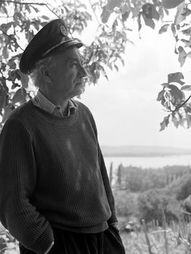 Illyés Gyula író, költő a tihanyi szőlőjében. Hajóskapitányok által hordott sapkát és pulóvert visel, zsebre dugott kézzel, oldalról fotózva; a háttérben a Balaton