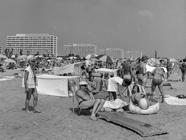 Mamaia, tengerpart. A háttérben kocka alakú szállodasor, az előtérben a parton napozó emberek.
