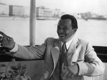 Jávor Pál színművész egy dunai hajón, háttérben a Széchenyi Lánchíd. Széles mosollyal, jobb kezével előre mutat