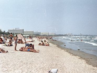 Mamaia, tengerpart. A háttérben betonszállodák, az előtérben a homokon napozó emberek.