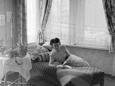 Egy nő könyvet olvasva fekszik az ágyon egy ablak előtt a lakásban 1942-ben.