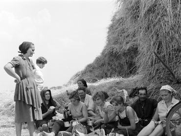 Ebédidejüket töltő mezőgazdasági munkások egy hatalmas szénabála árnyékában ülnek 1964-ben.