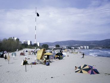 Bulgária, Napospart. A néptelen tengerparton napernyők, a háttérben hegyek, szállodák és a tenger