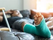 Csonttörés a lábfejben és a lábszárban egy férfi páciensnél, sínekkel rögzített gipsszel és mankókkal, a műtét utáni rehabilitáció és az ortopédiai gyógyulás ideje alatt, otthoni ápolás mellett