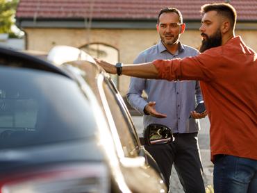 Két férfi egy autó mellett állva intéze a jármű adásvételét