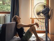 Egy hőgutától szenvedő fiatal nő otthon a padlón ül egy ventilátor előtt