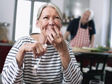 Egy idős nő boldogan nevet miközben eszik a konyhában