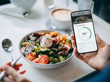 Közelkép egy fiatal nőről, aki okostelefonján egy fitneszalkalmazást használ, hogy személyre szabja napi étrendjét, és ellenőrzi a marhahúsos Cobb-saláta tápértékét és kalóriatartalmát. A kiegyensúlyozott étrend fenntartása. Egészséges étkezési szokások