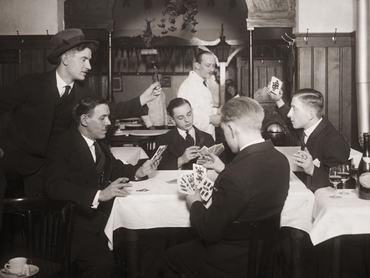 férfiak ülnek körül egy fehér abrosszal letakart asztalt, közben kártyáznak (1930)