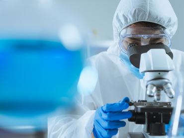 Egy fiatal, jóképű ázsiai tudós a laboratóriumban beállítja a fókuszt, és mikroszkóppal vizsgálja a sejtek biokémiai szerkezetét. Orvosok és tudósok dolgoznak a koronavírus-járvány idején a laboratóriumban – a COVID-19 témájában