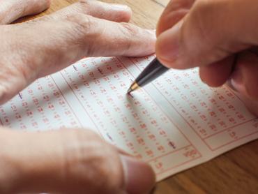 Egy kéz közelről ahogy tollal kitölt egy lottószelvényt