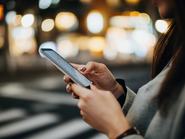 Közelkép egy nőről, aki éjszaka egy forgalmas városi utcán okostelefonjával keresi az útját