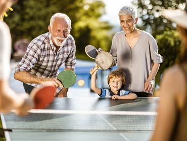 Boldog nagyszülők a fiú unokájukkal vidáman pingpongoznak a kertben a gyerek szüleivel