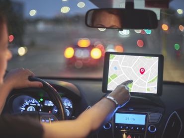 Hátulnézet egy autót vezető nőről, aki a navigációs rendszer érintőképernyőjét érinti