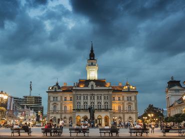 Novi Sad, Szerbia, este a város főterén, emberek sétálnak és üldögélnek
