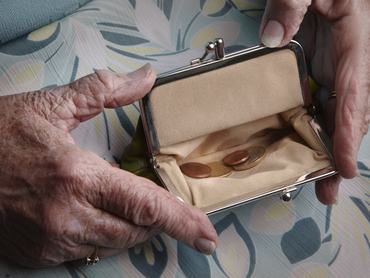 Egy idős nő ráncos kezében tart egy pénzérméket tartalmazó pénztárcát