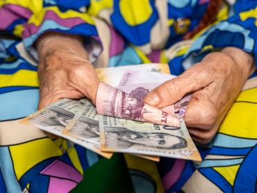 Egy idős asszony ráncos kezében tartja a nyugdíjként kapott forint bankjegyeket