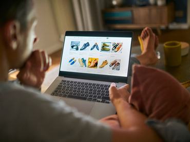 Egy férfi a laptopja képernyőjén nézi egy webáruház kínálatát a nappalijában