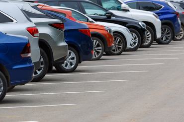 Különböző színű autók sora egy aszfaltos parkolóban egy felhős nyári napon, szelektív élességgel