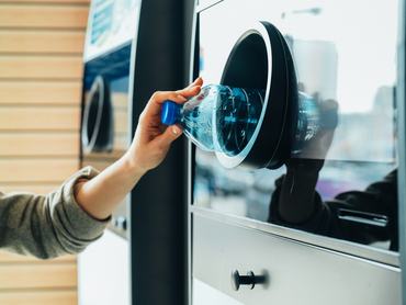 Egy nő műanyag palackot tesz az üvegvisszaváltó automata nyílásába