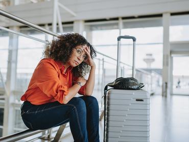 Egy nő fáradtan várakozik a bőröndje mellett ülve a repülőtéren