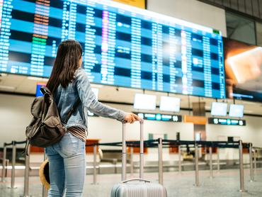 Egy fiatal női turista a budapesti repülőtér érkezési és indulási tábláját nézi.