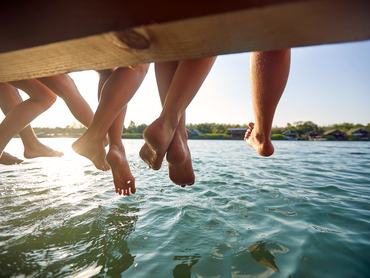 Stégen ülő fiatalok lábai a víz fölött egy strandon