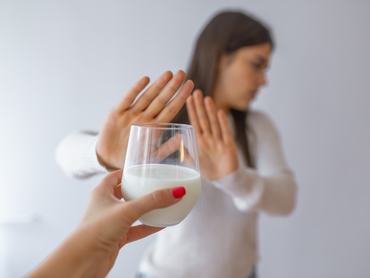 Laktózérzékenység, a tejtermékekkel kapcsolatos egészségügyi probléma. Egy pohár tejet tartó nő, akit erős hasfájás gyötör. Egy fiatal nő, aki nem hajlandó tejet inni