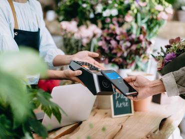 Egy fiatal nő bankkártyával, érintésmentes fizetéssel vásárol egy virágcsokrot a virágboltban
