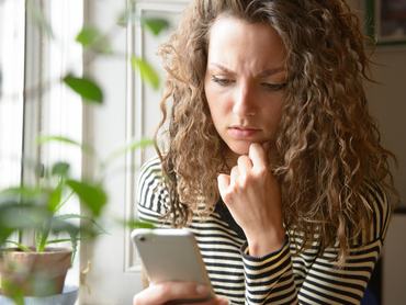 Egy fiatal nő aggódva nézi a kezében tartott telefonját